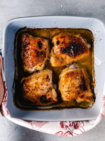 four baked chicken thighs in square blue dish being held with kitchen towel