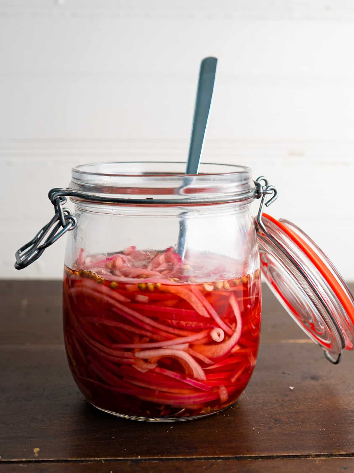 a ring top mason jar with quick pickled onions and a spoon. the colour is pink due to the red onions. 