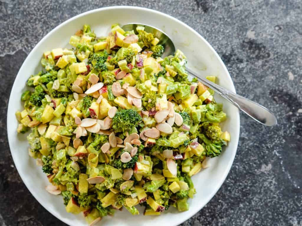 Broccoli salad on white plate with spoon on stone background