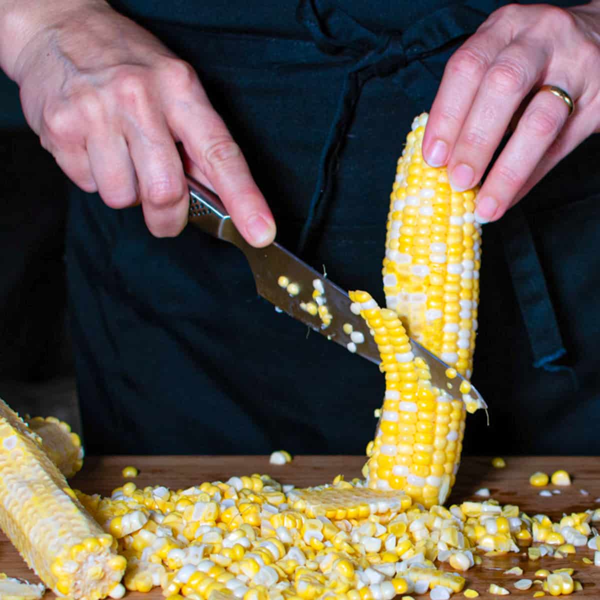 cob of corn standing up right with a knife cutting down to remove kernals.