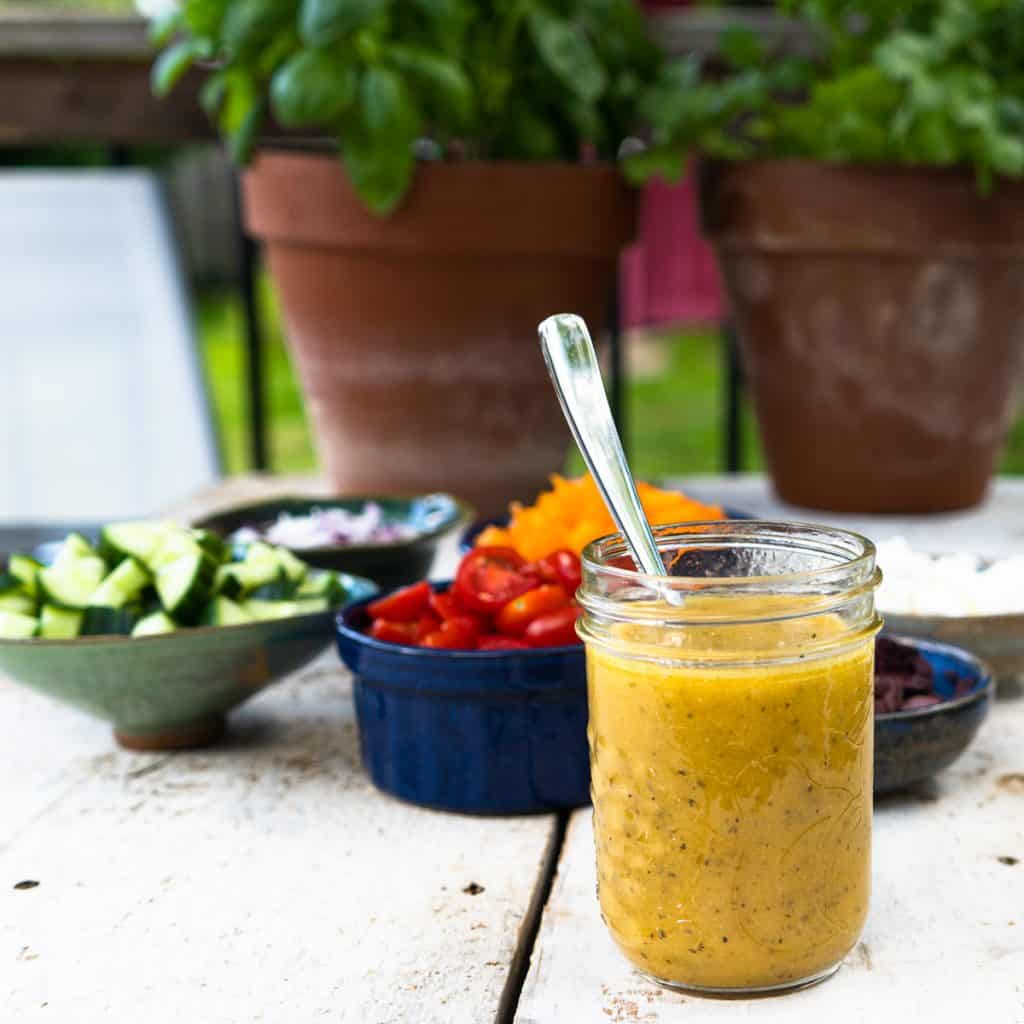 Greek salad dressing in mason jar with salad ingredients in background