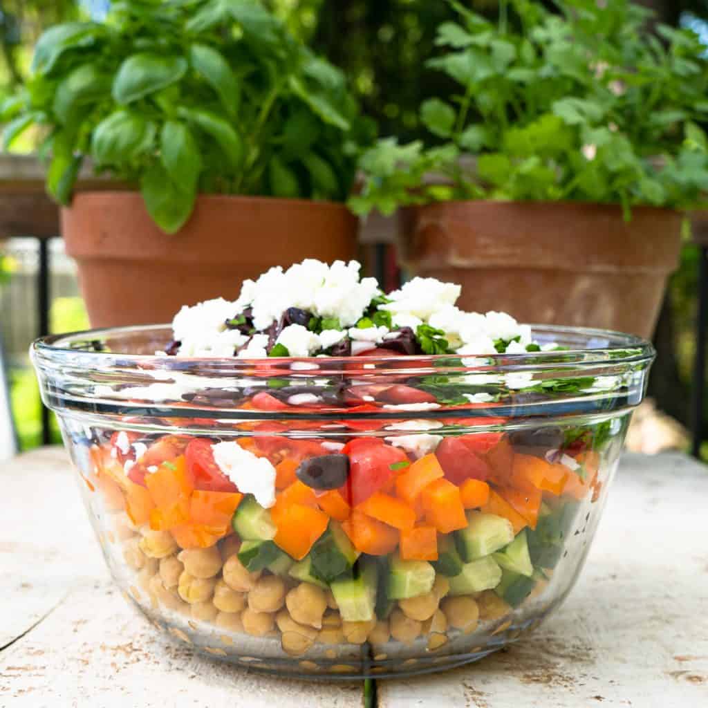 all salad ingredients in glass bowl with fresh herbs in background