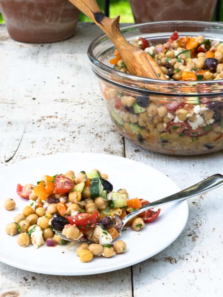 one serving chickpea salad on white plate with large bowl of salad in background