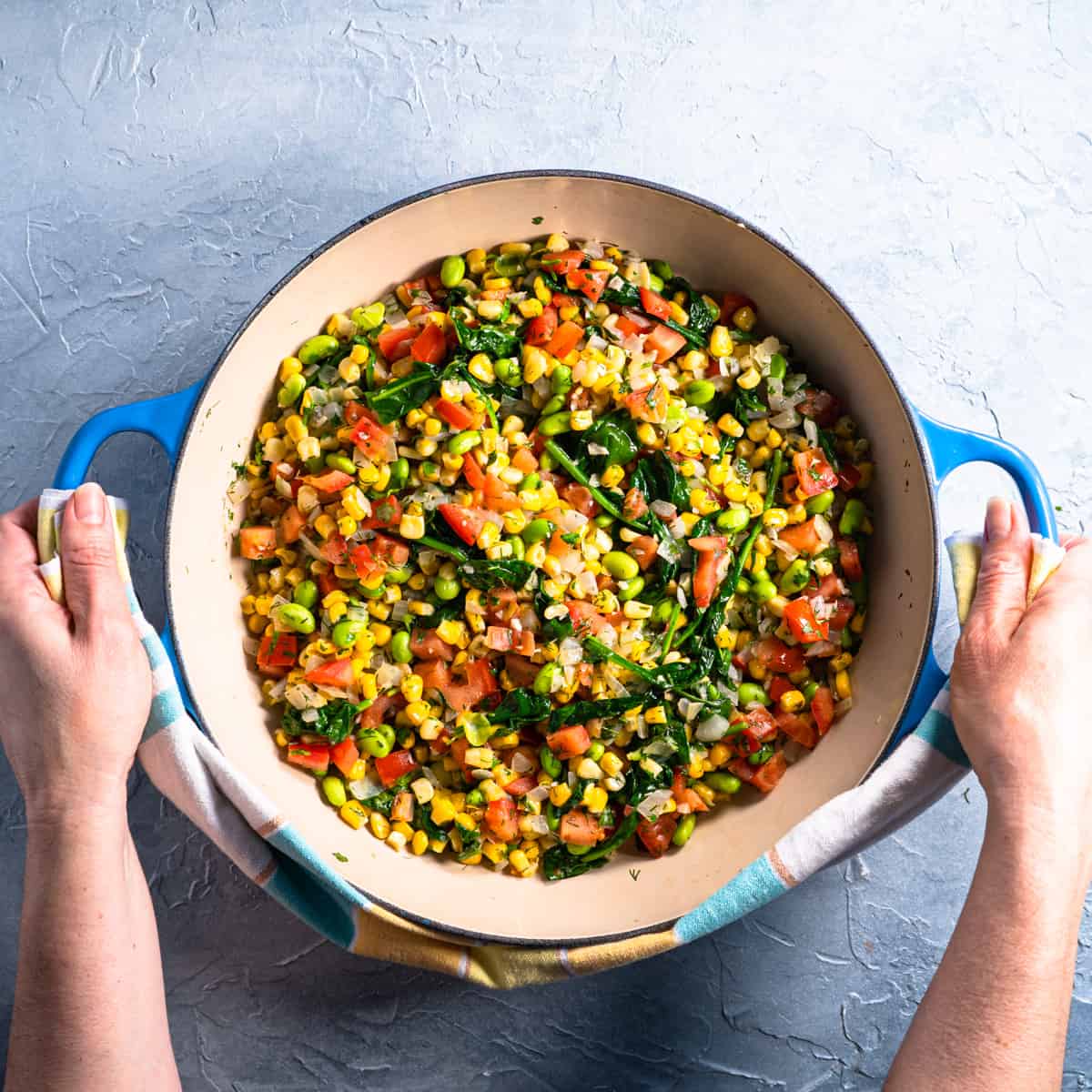 summer succotash being held in blue casserole dish showing hands.