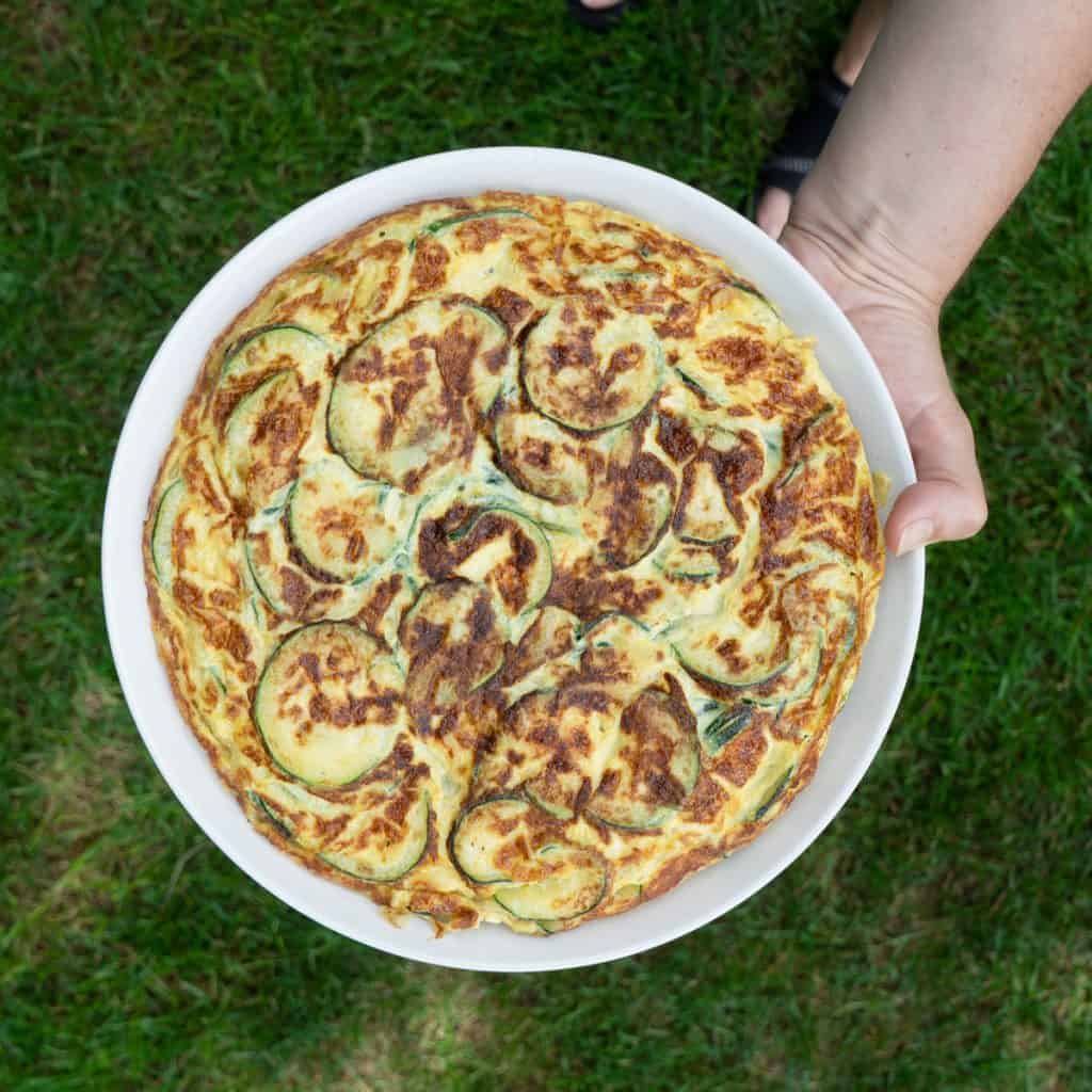 Spanish zucchini omelette finished on white plate held over grass