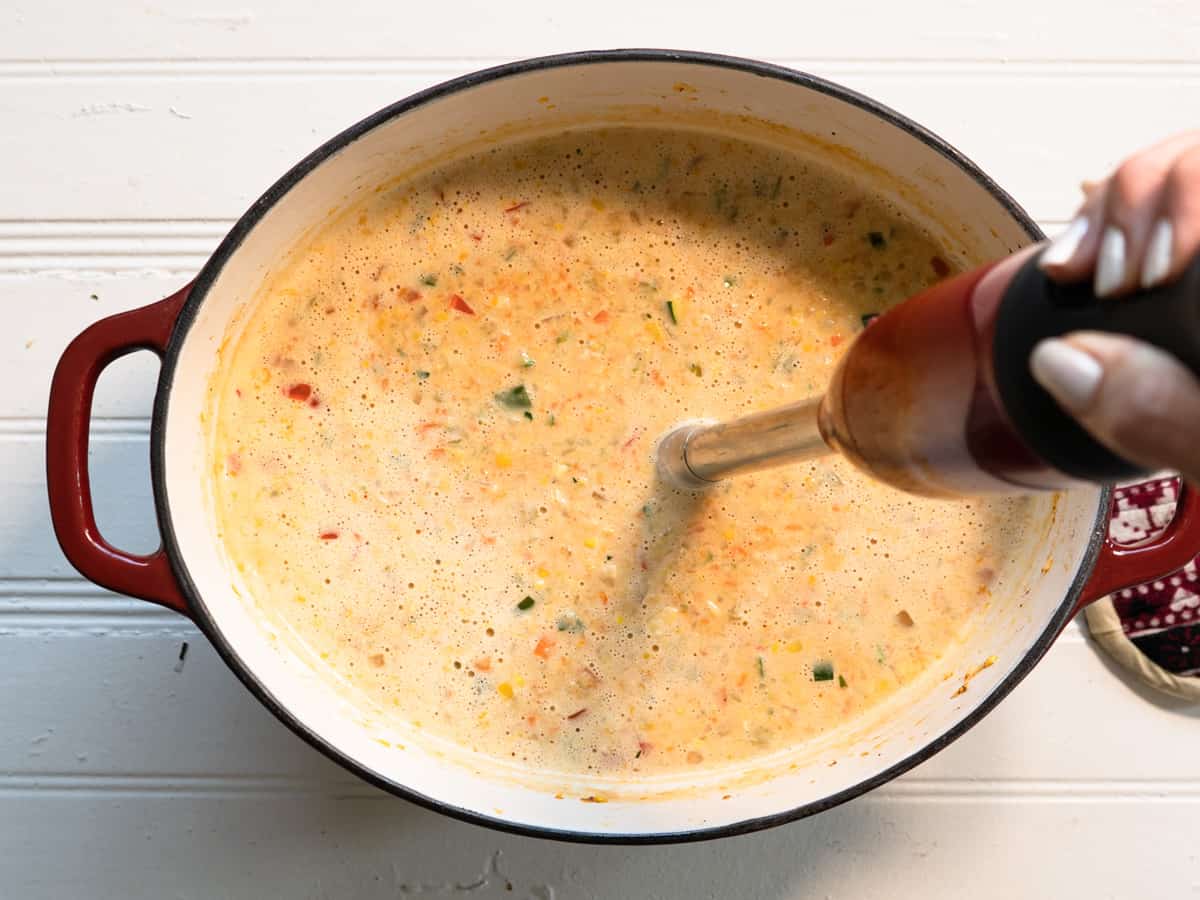 Oval pot of soup with hand blender blending soup