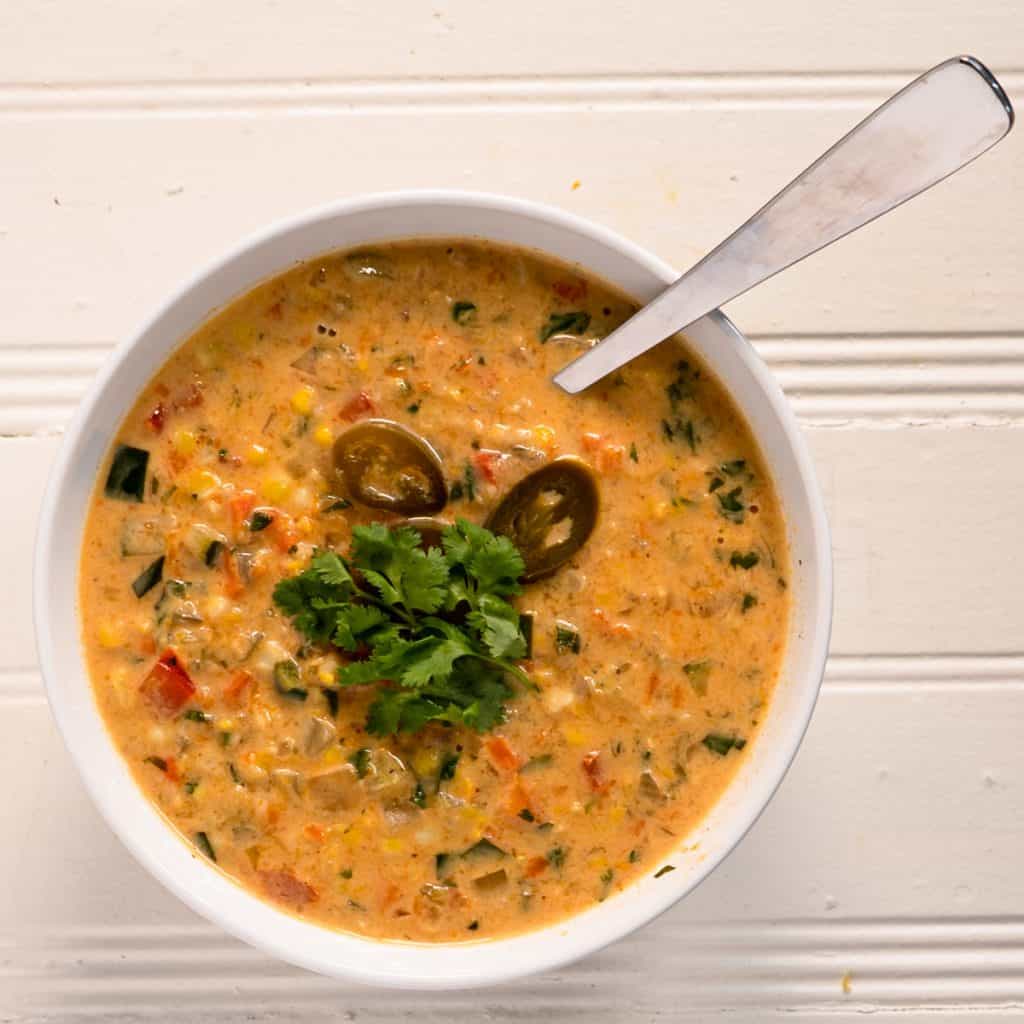 single white bowl of soup with spoon. garnished with jalapeno peppers and cilantro