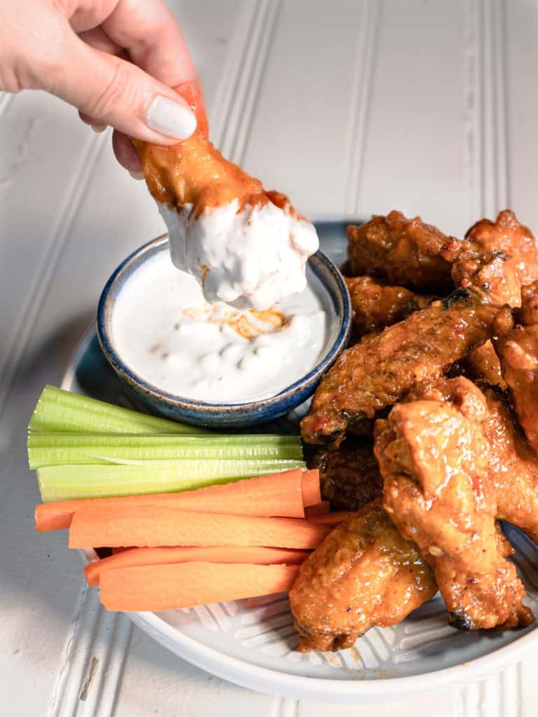 buffalo wings on a plate with carrot and celery stick and blue cheese dip. one wing being dipped