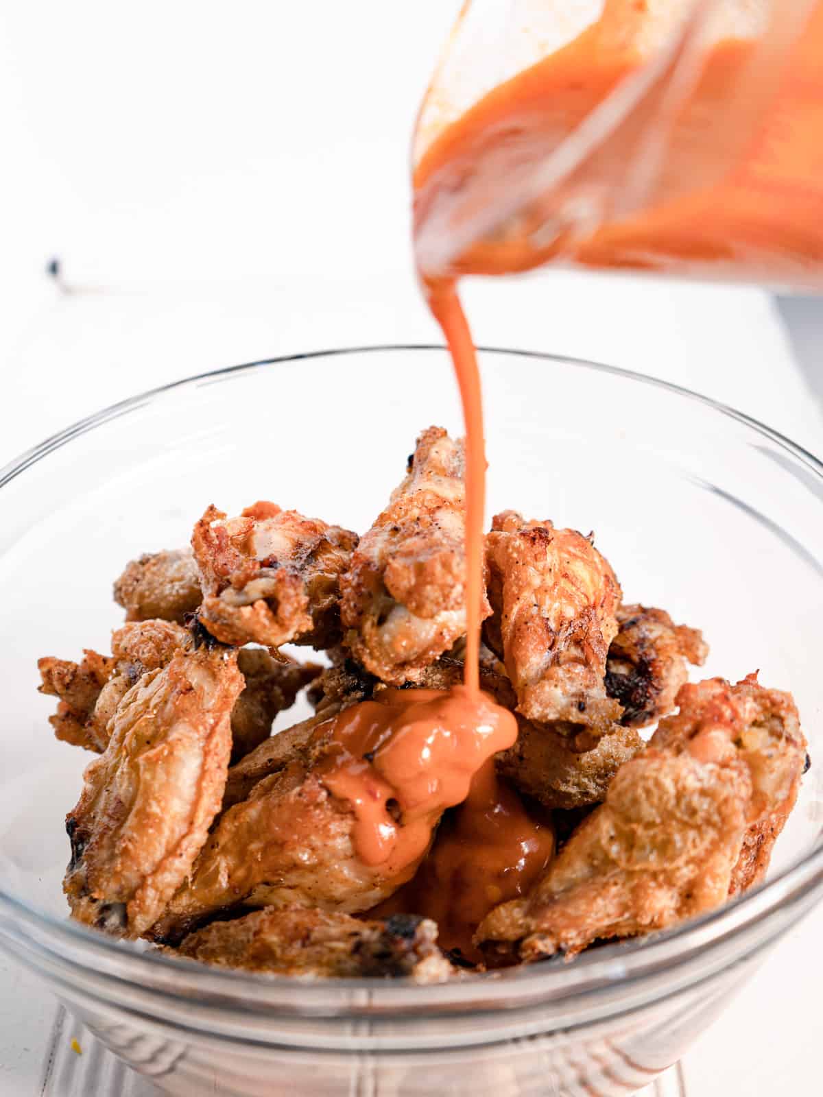 a glass bowl of wings with sauce being poured over top.