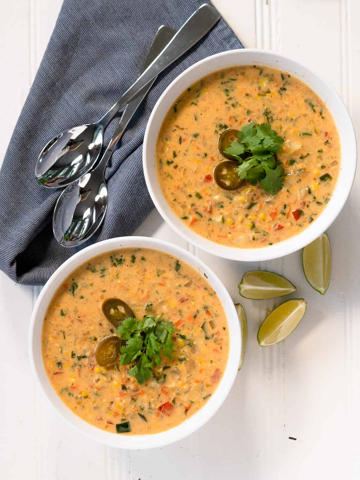2 white bowls of prepared soup topped with cilantro and jalapenos. Lime wedges on the side.