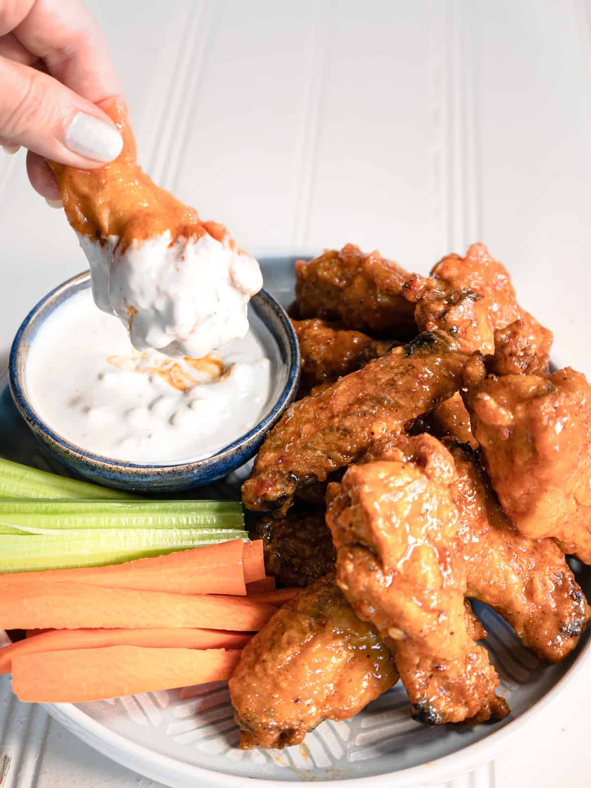 buffalo wings on a plate with carrot and celery stick and blue cheese dip. one wing is being dipped into the sauce.