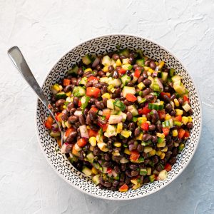 black bean salad in a black and white bowl with spoon on light grey background