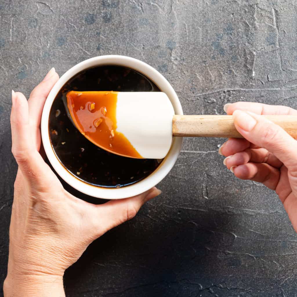 teriyaki sauce in a white bowl with white rubber spatula held in hands