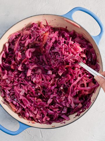 Braised red cabbage cooked and in a blue dish. Hand holding a spoonful of cabbage