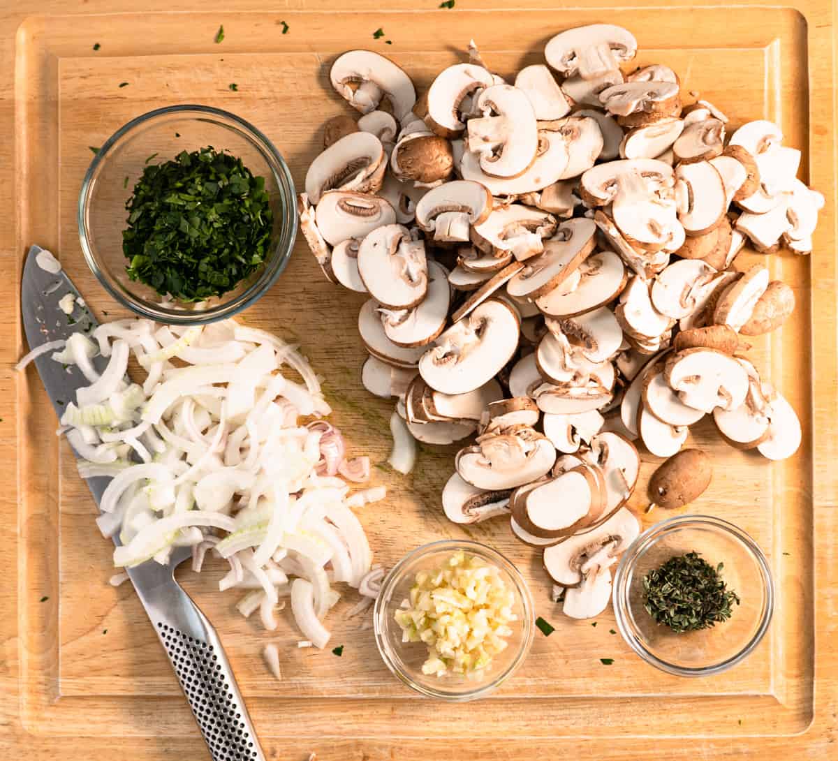 Prepared mushrooms, onions, garlic and herbs on a wood cutting board