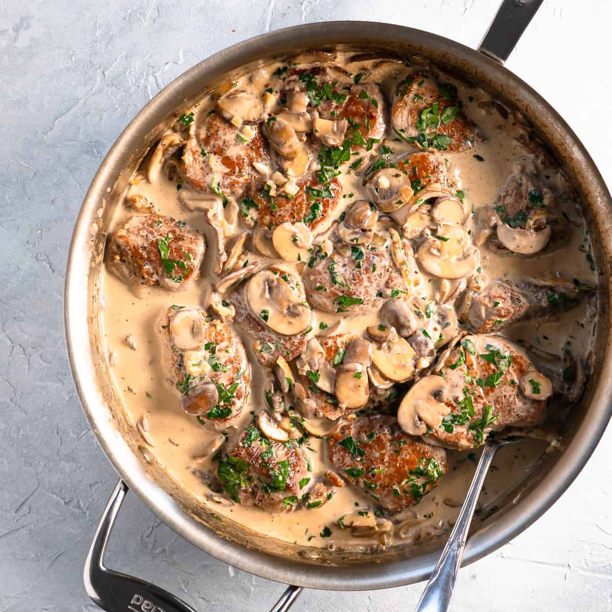 pork medallions in creamy mushroom sauce in pan with spoon.