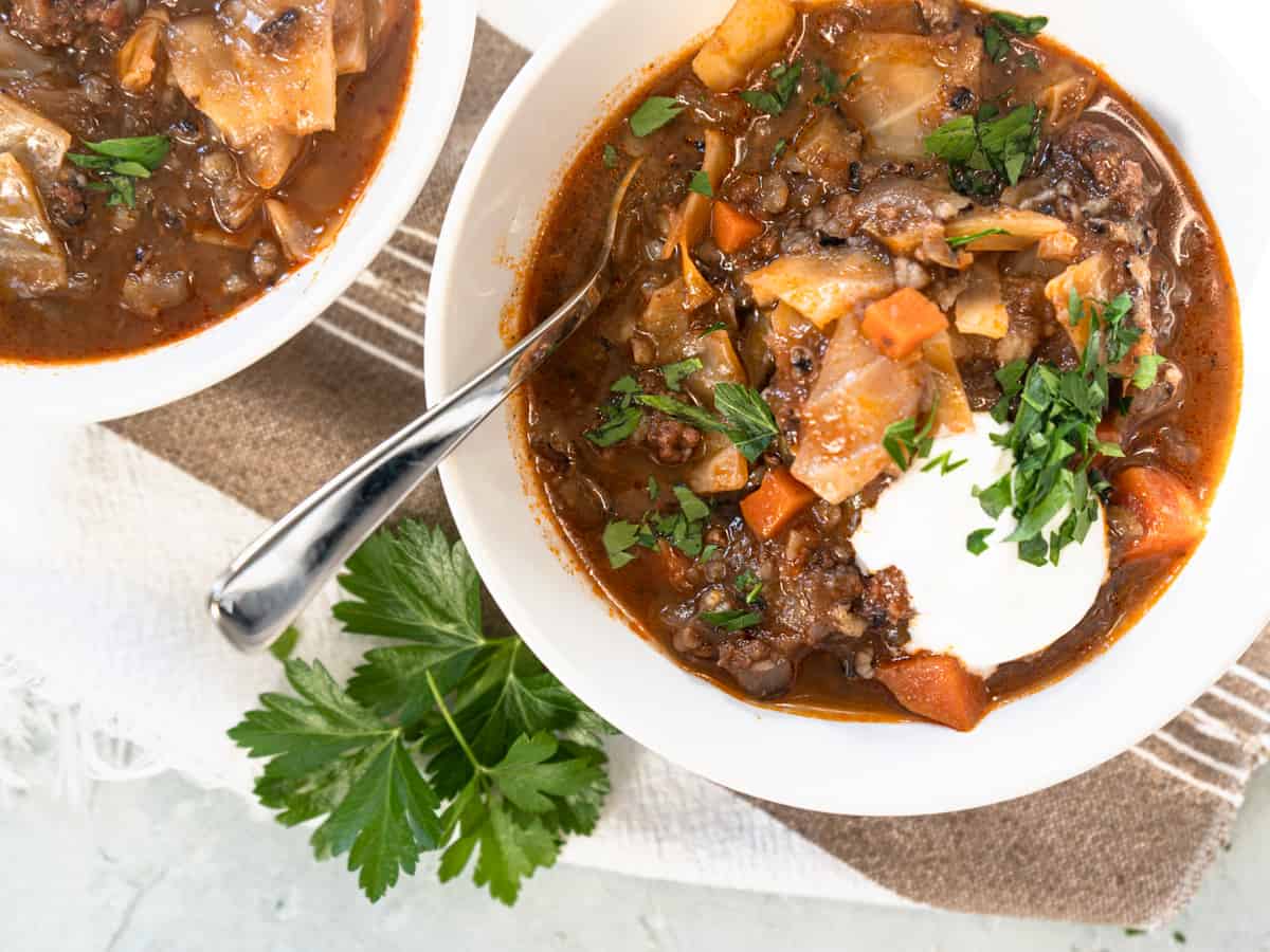 cabbage roll soup in white bowl topped with sour cream and fresh parsley