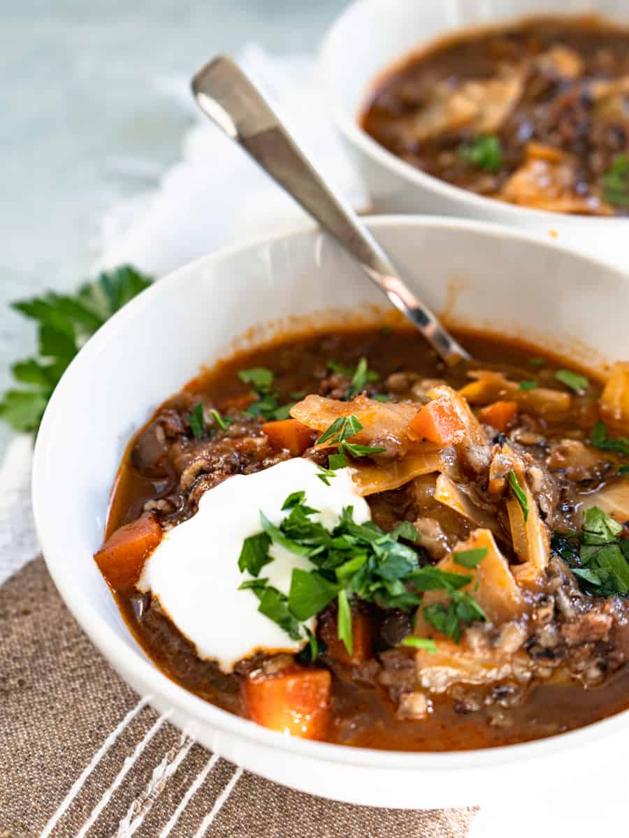 cabbage roll soup in white bowl topped with sour cream and fresh parsley