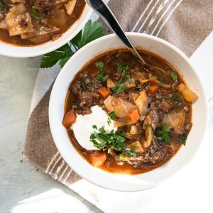 cabbage roll soup in white bowl topped with sour cream and fresh parsley