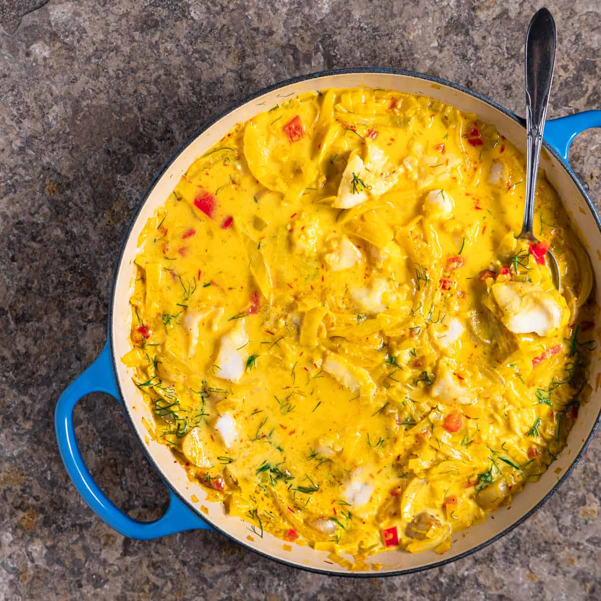 Full, blue casserole dish of fish stew with fennel and saffron