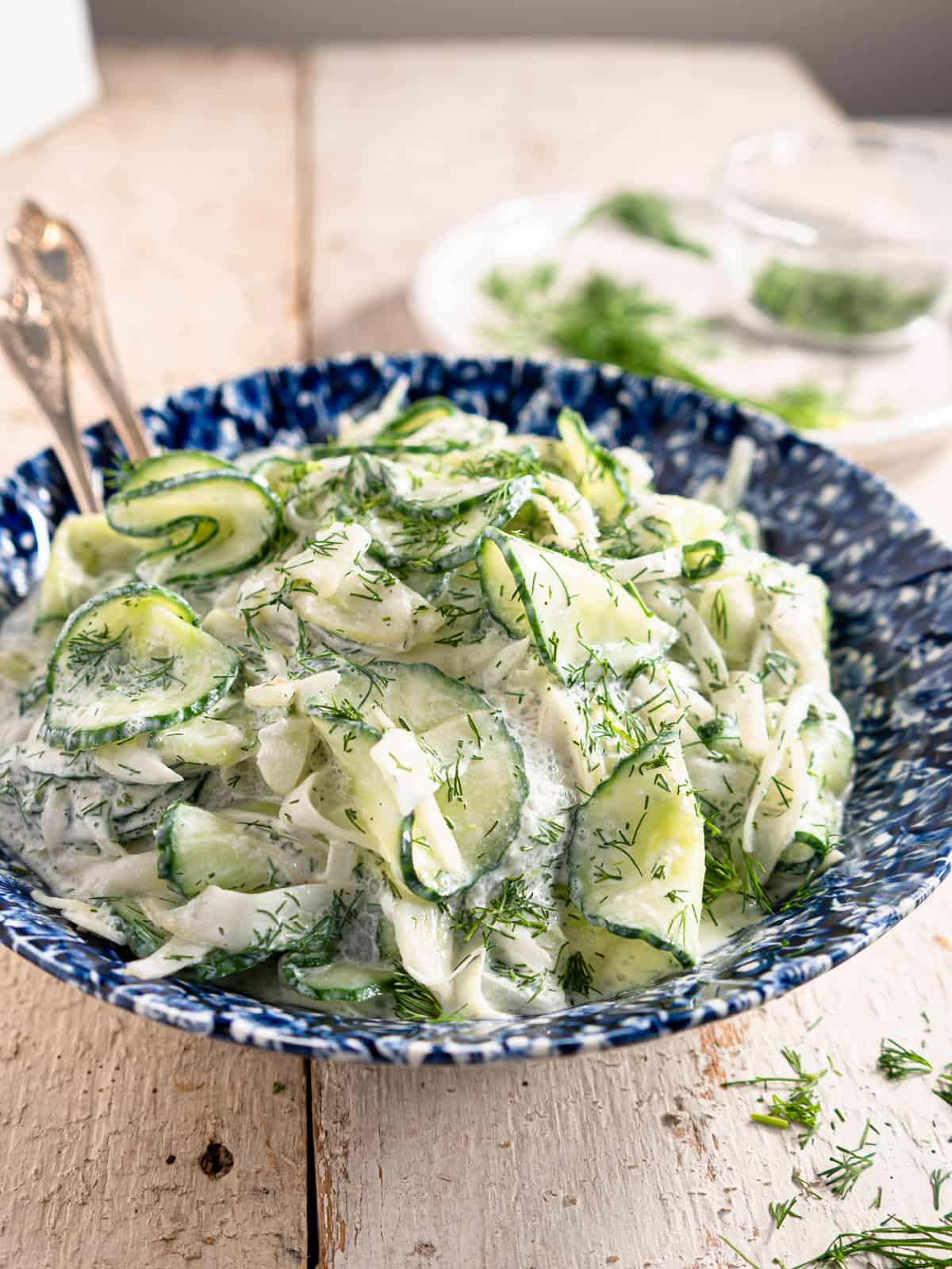 cucumber and fennel salad in a blue and white bowl with serving utensils. 