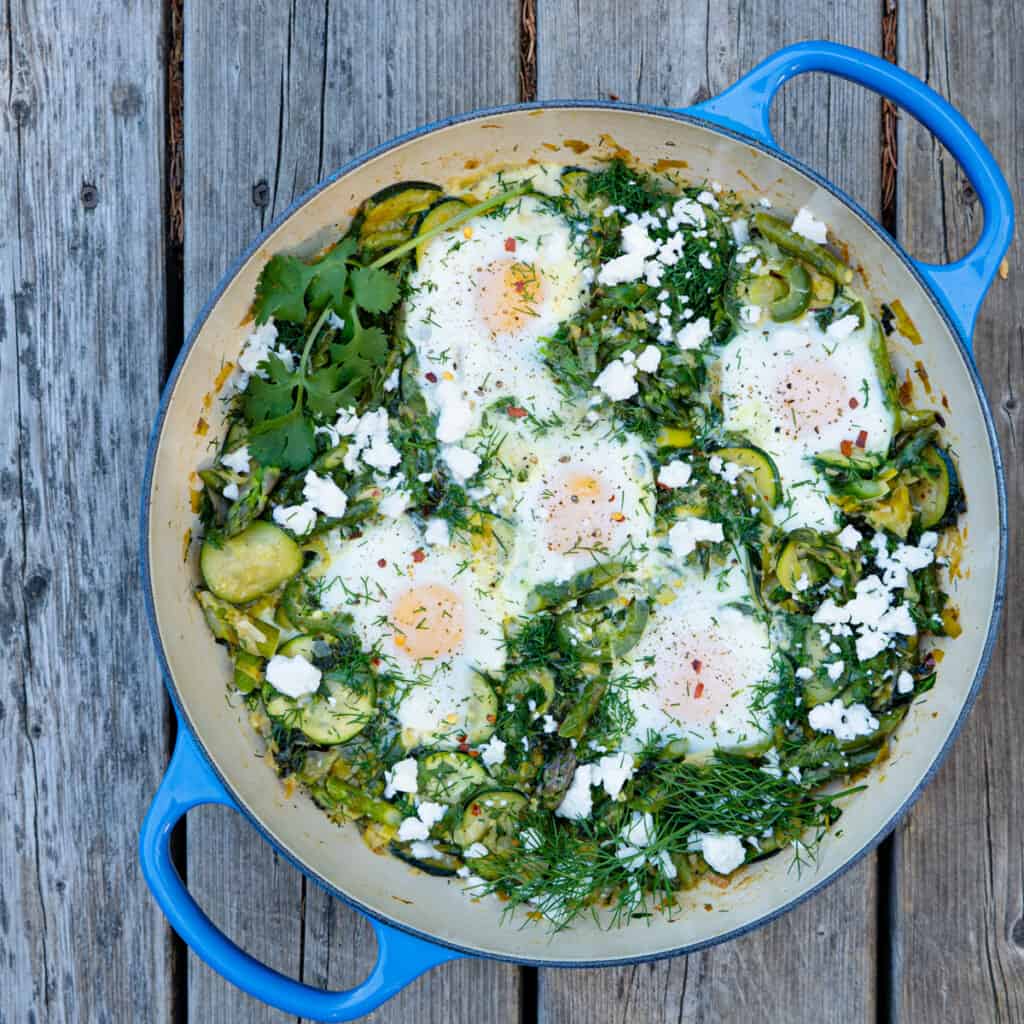 green shakshuka in blue casserole dish on wood background