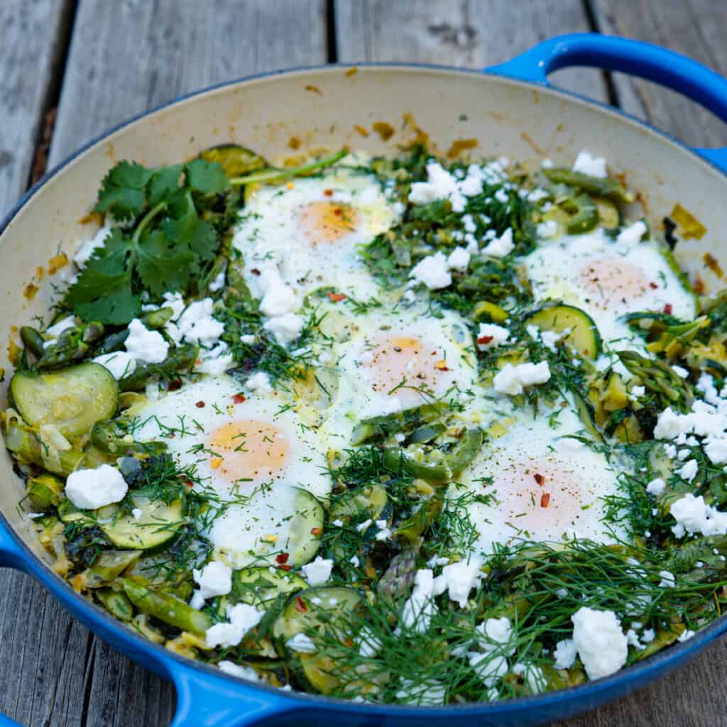 Green shakshuka in a blue casserole on wood background