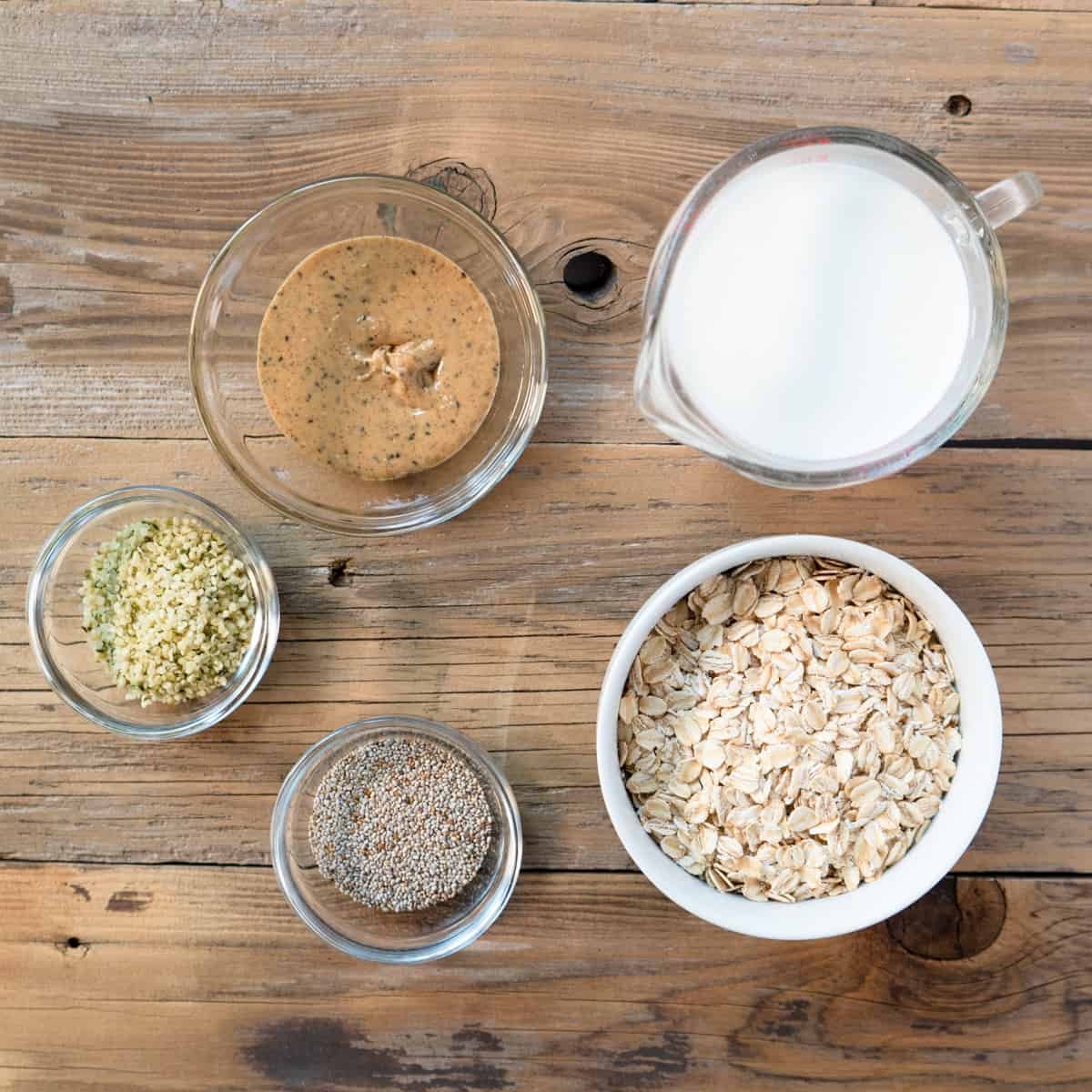 ingredients needed to make overnight oats displayed in bowls on a wood background. 