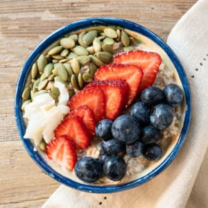 one bowl of high protein overnight oats topped with fresh fruit, seeds, and coconut.