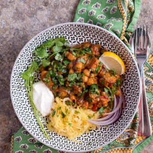 Single serving of tempeh and chickpea curry garnished with sliced red onions, yogurt, and a lemon wedge.