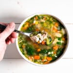 turkey and vegetable soup in a white bowl on white board background holding a spoon