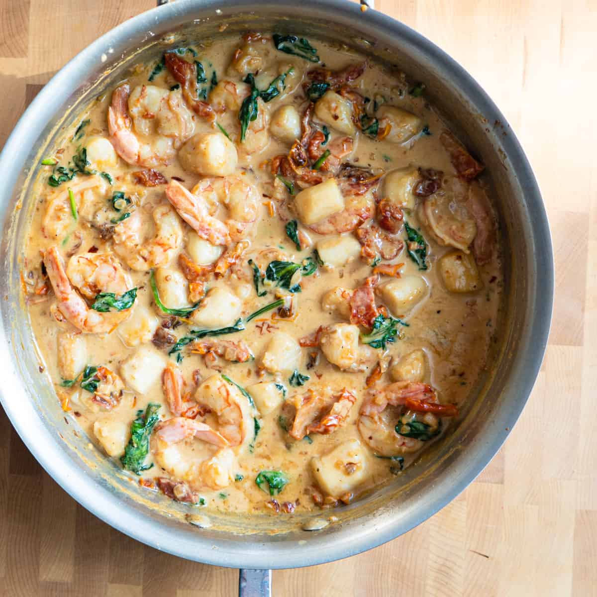 creamy shrimp and scallops with sundried tomatoes and spinach in metal pan.
