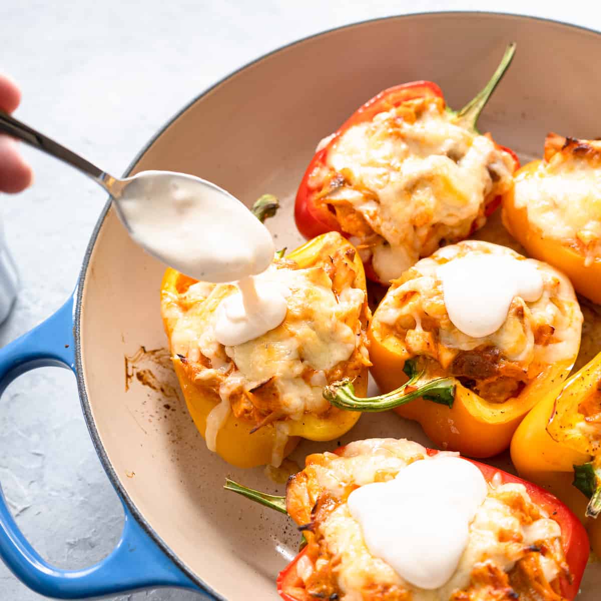 Buffalo chicken stuffed peppers in a baking dish with spoon pouring blue cheese sauce