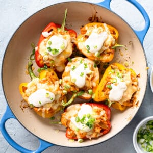 buffalo chicken stuffed peppers in a blue baking dish topped with blue cheese dressing