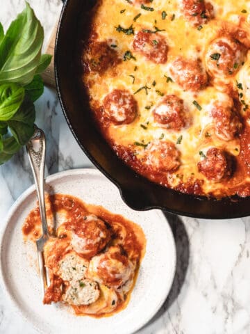 chicken parmesan meatball skillet in background with 3 meatballs on a plate with a fork.