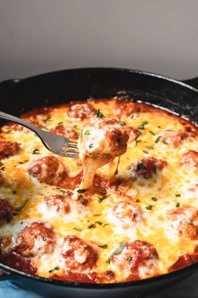 close up of one meatball being lifted with a fork showing gooey cheese