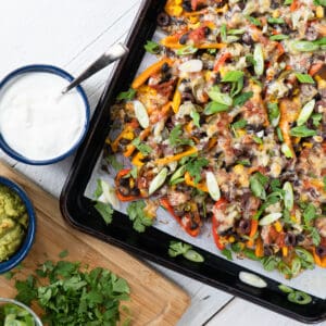 a tray of mini pepper nachos garnished with sliced green onions and fresh cilantro and a side dish of sour cream