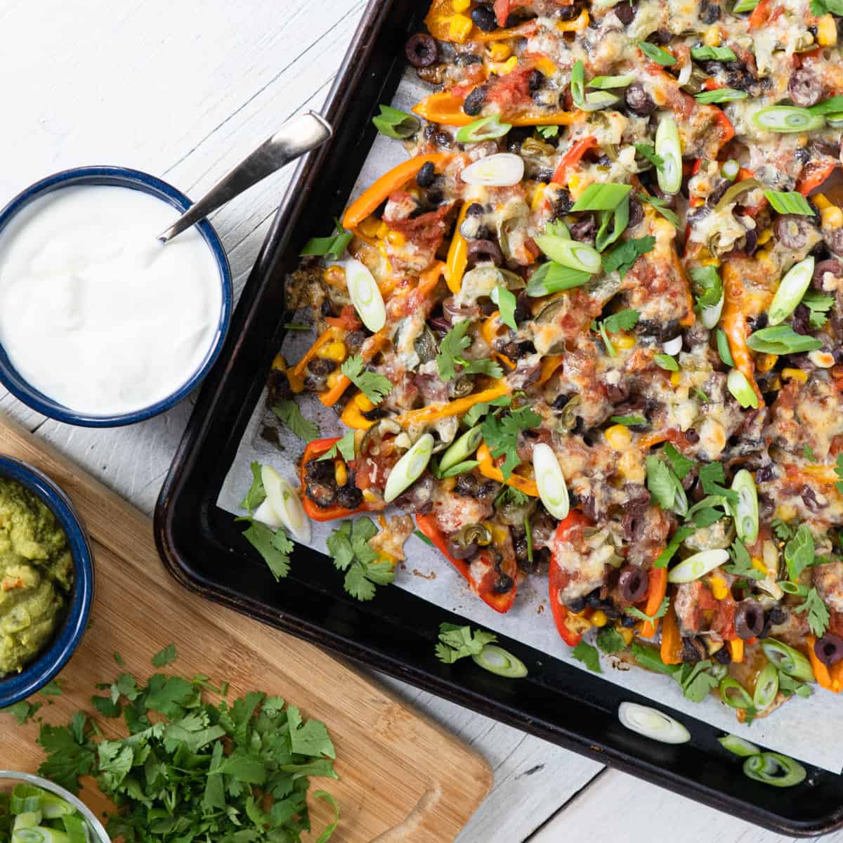 a tray of mini pepper nachos garnished with sliced green onions and fresh cilantro and a side dish of sour cream 