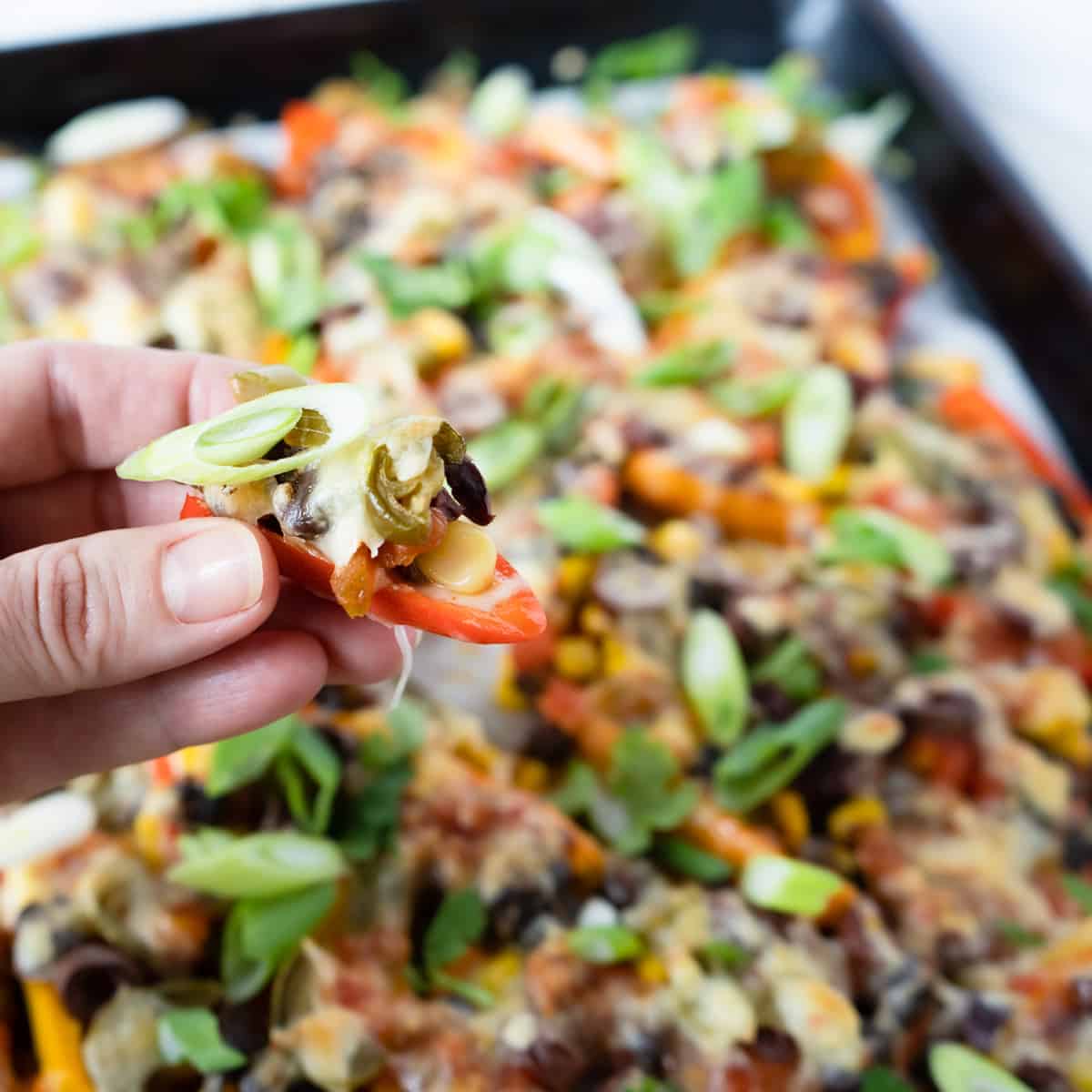 close up of a person's hand holding a mini pepper nacho