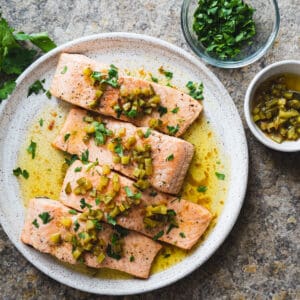 roasted salmon with brown butter pickle sauce on white plate with side dishes of parsley and pickle sauce