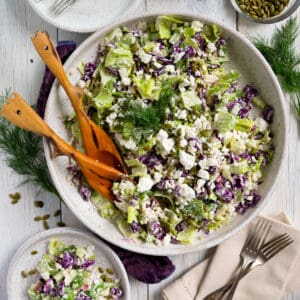 the completed dill pickle salad on a white platter with wooden serving utensils.