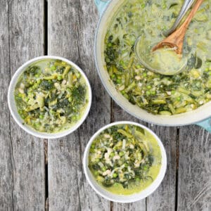 Two bowls of green minestrone soup with the pot on the side.