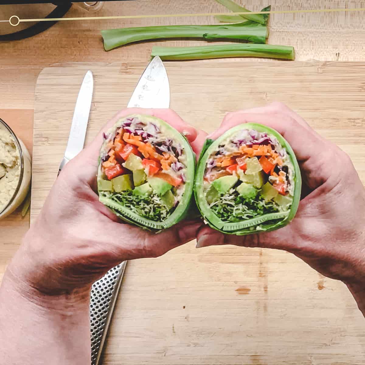 collard wrap cut in half. 2 hands holding one in each showing colourful fillings. 