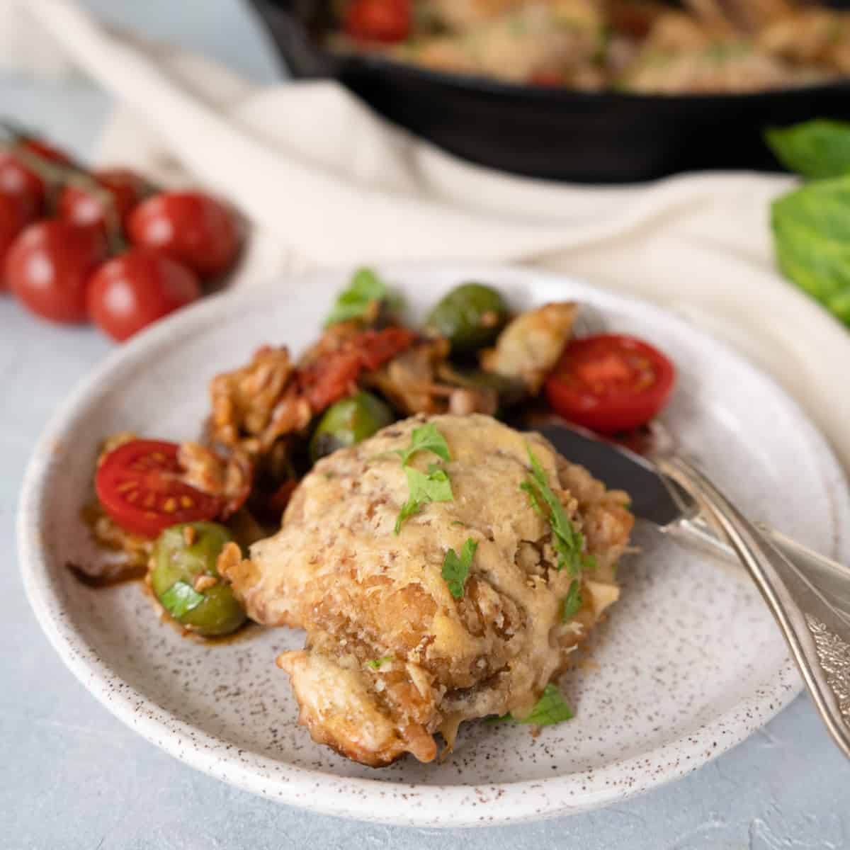 one chicken thigh with vegetables on a white ceramic plate. 