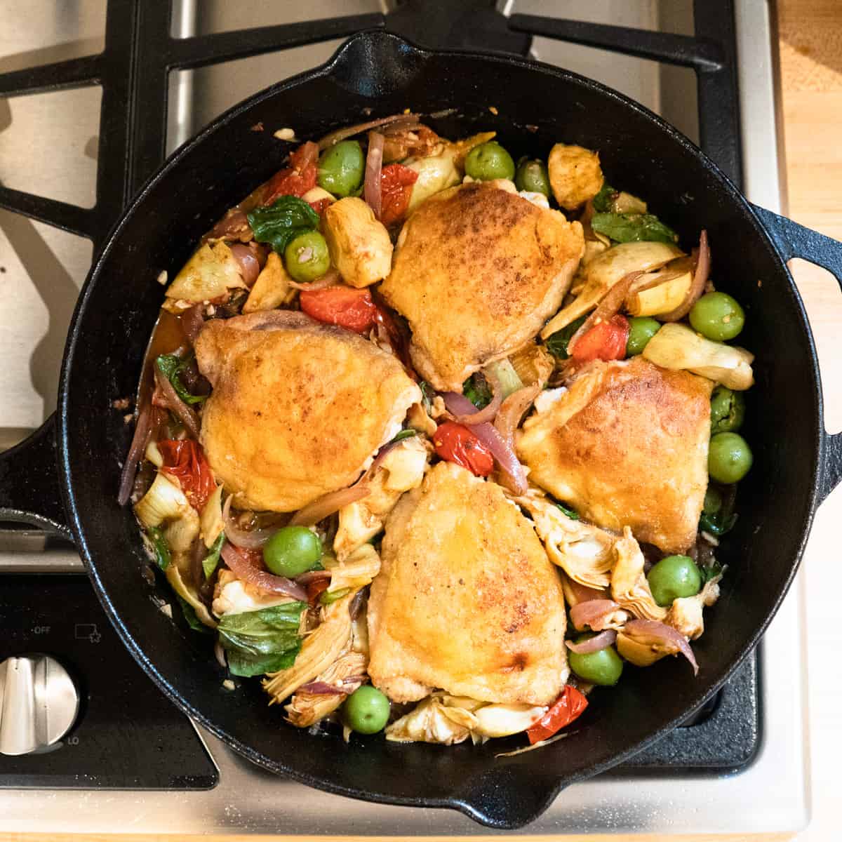 Cooked vegetables and browned chicken thighs in a skillet ready for the oven. 