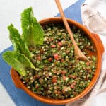 finished quinoa tabbouleh in a clay dish garnished with lettuce leaves.