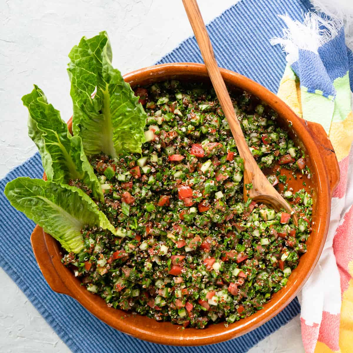 finished quinoa tabbouleh in a clay dish garnished with lettuce leaves.