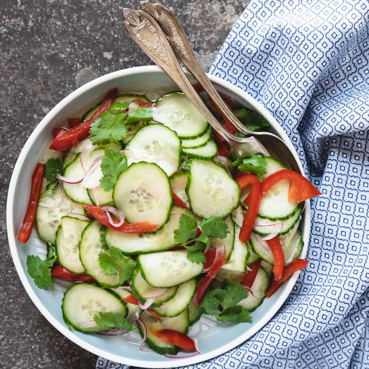 finished cucumber salad on a serving plate with serving utensils.