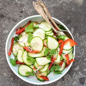 finished cucumber salad on a serving plate with serving utensils.