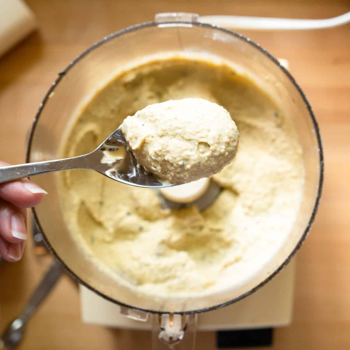 Hummus in food processor after pureeing with a close up of a spoonful.